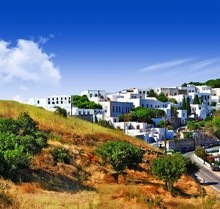 Scenic View of the Island of Patmos in Greece with windmills, rolling hills, blue skies, and buildings.