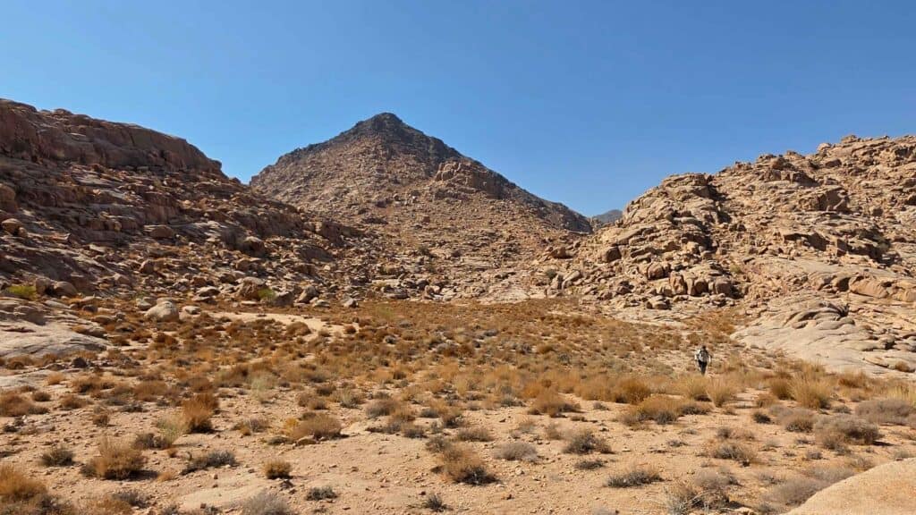 A lone climber crosses the open ground of the plateau of the seventy elders, with the peak of Jabal Maqla rising ahead.