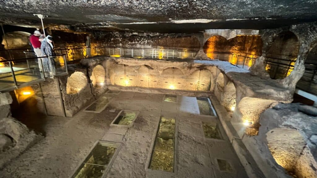 Interior of the gallery grave at Dara, southeastern Turkey, showing arched burial niches cut into the rock walls and glass floor panels over the chamber below.