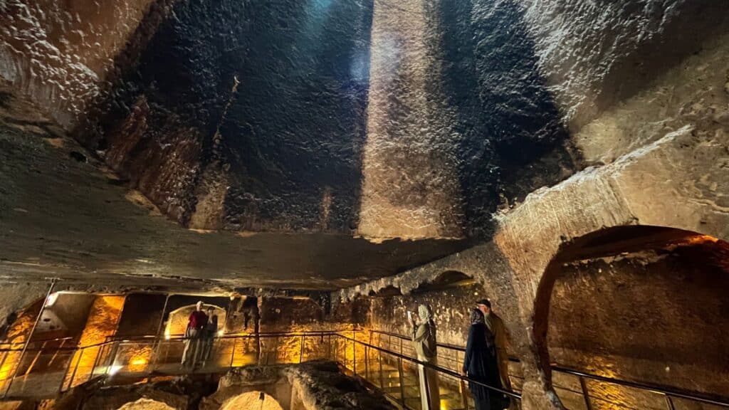 Interior of the rock-cut gallery grave at Dara, southeastern Turkey, with visitors on a raised walkway.