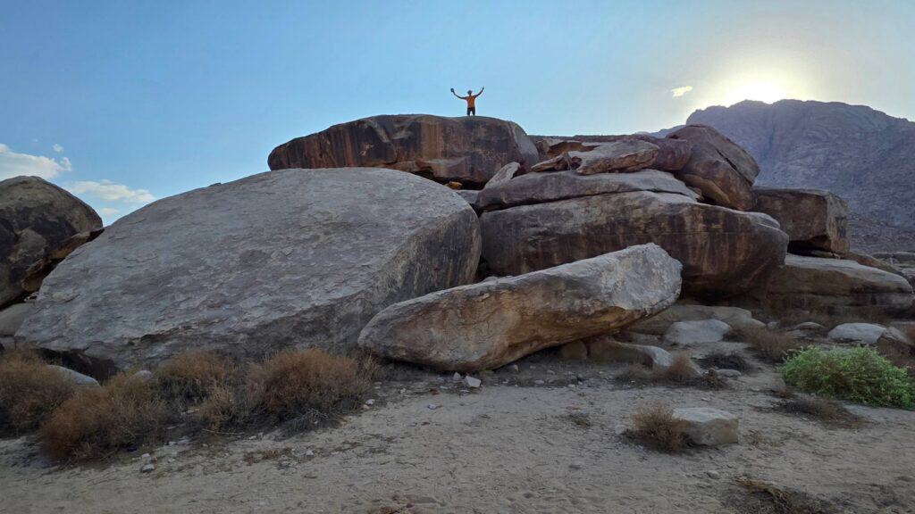 A man standing on the flat top of the golden calf altar outcrop below Jabal Maqla, showing the height of the boulder formation above the surrounding plain